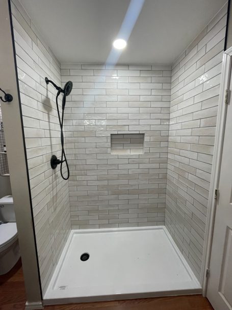 New Shower Valve in San Angelo TX Modern shower with white tiled walls, a black showerhead, and built-in shelf.